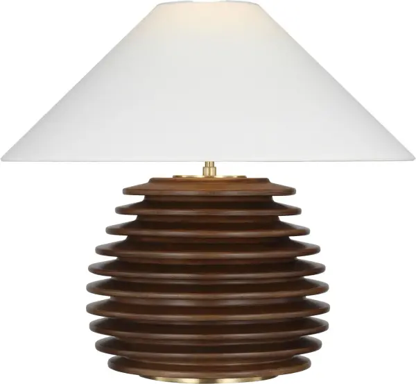 The Crenelle table lamp features a distinctive stacked wood construction in burnished birch, creating architectural interest with natural texture. The 20-inch height and linen shade provide warm, diffused lighting ideal for living spaces.