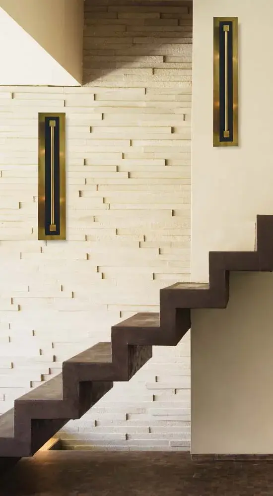 The Louvre sconce combines warm antique brass with modern matte black in a striking 22-inch vertical design. Its distinctive louvre detailing creates visual interest while providing elegant ambient lighting for hallways and living spaces. - alternate view