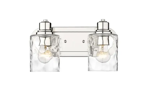 The Lumley 2-Light Bath Sconce combines polished nickel finish with hand-blown clear optic glass for timeless bathroom elegance. Its compact 13.75" width fits most vanity spaces while providing ample illumination.