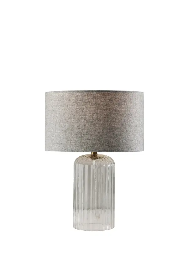The Carrie Small Table Lamp blends coastal charm with contemporary elegance through its clear ribbed glass base and antique brass neck. The soft-touch grey drum shade provides gentle illumination perfect for bedside or desk use.