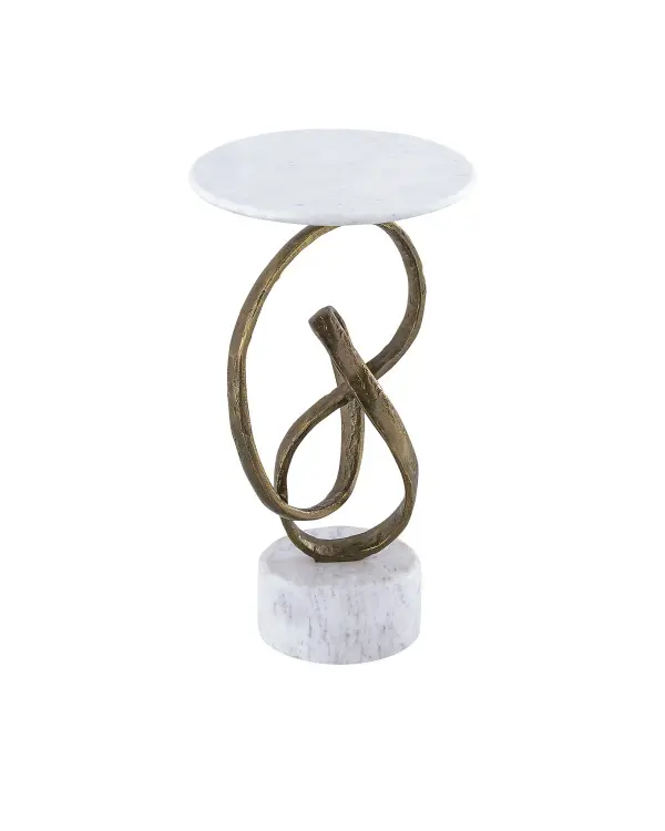 A striking contemporary accent table featuring a cast aluminum ribbon in antique brass that curves dramatically from a white marble base to support a thin marble top. The masculine design balances rough luxe texture with refined materials.