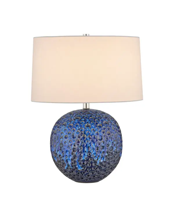 A striking artisanal table lamp featuring hand-carved ceramic with a moonscape-inspired texture and reactive blue glaze. Each piece is unique with organic variations, making it a sculptural statement for contemporary interiors.