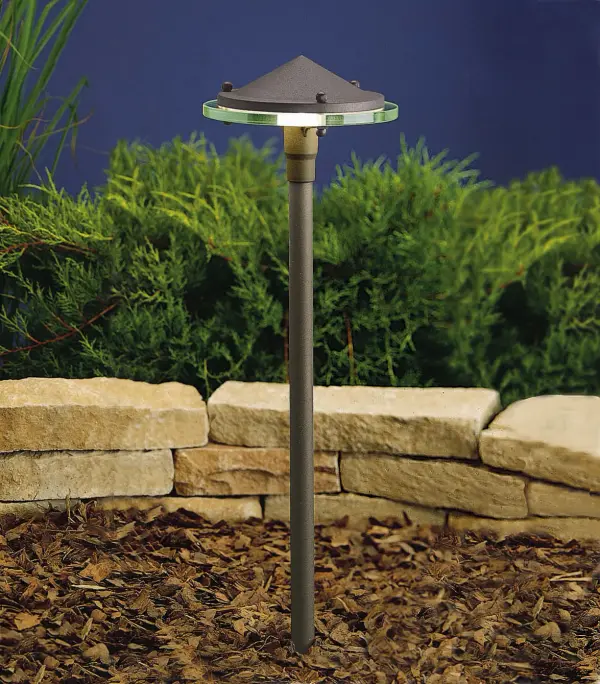 A modern landscape fixture that combines clean architectural lines with functional outdoor lighting. The textured bronze finish and clear glass create subtle sophistication for pathways and garden beds.