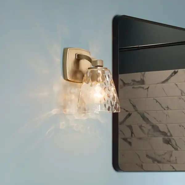 The Marant wall sconce combines clean contemporary lines with warm champagne bronze finish and textured clear water glass. Its compact 5-inch width makes it ideal for tight spaces while delivering full ambient glow.