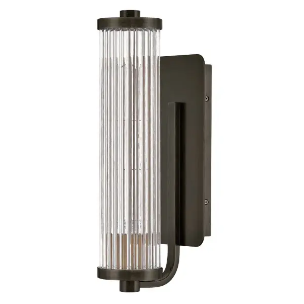 A touch of modern style and vintage charm, Ellery’s Clear glass shade is composed of tall cylindrical glass rods, creating a beautiful reeded effect when illuminated. A large rectangular backplate and matching end caps are finished in a Black Oxide, Heritage Brass, or Polished Nickel finish that complements any bath or living space. - alternate view