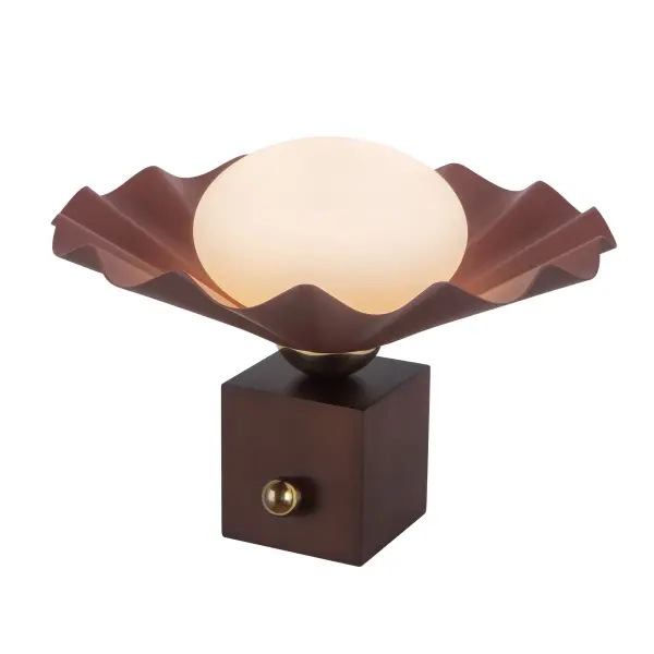 The Furrow Table Lamp by Jason Koharik transforms functional lighting into a work of art. Inspired by rare pearls and ocean shells, this 12-inch piece features a sculptural pine green metal base with walnut wood accents and an opal glass diffuser that creates soft, inviting illumination.