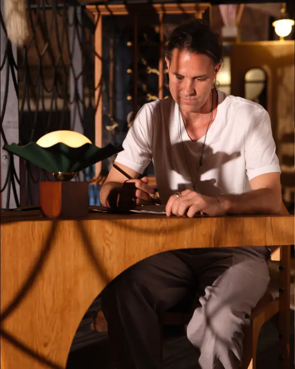 The Furrow Table Lamp by Jason Koharik transforms functional lighting into a work of art. Inspired by rare pearls and ocean shells, this 12-inch piece features a sculptural pine green metal base with walnut wood accents and an opal glass diffuser that creates soft, inviting illumination. - alternate view