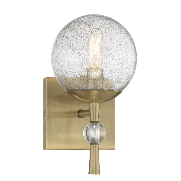 The Populuxe bath lamp combines industrial-modern aesthetics with artisanal craftsmanship. Its oxidized aged brass finish and unique volcanic glass shade create dramatic light diffusion perfect for contemporary bathrooms.