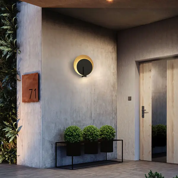 The Eclipse LED Wall Sconce combines striking visual artistry with practical outdoor lighting. Its moon-eclipse design creates a captivating backlit effect while integrated downlighting provides functional illumination. - alternate view