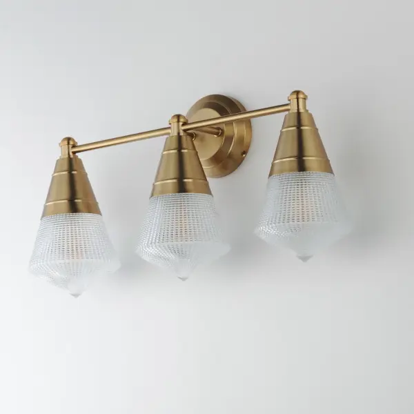 A prismatic diffusion of light is housed within pressed cone glass shades. Choose from pendants with tapered metal halves that conceal the light source or glass shades that are supported by a metal ring. Coordinating bath vanity lights complete the collection. Collection: Hargreaves Finish: Natural Aged Brass Glass: Prairie Rib Frost Width: 24.00" Height: 12.00" Weight: 7.40 lb Extension from Wall: 7.00" Wire: 8" Canopy: 5"x5" Number of Bulbs: 3 Maximum Wattage: 60.00 W Bulb Type: A19 Bulb Base: E26 Medium Light Source: Incandescent Dimmable Voltage: 120.00 V Material: Steel, Glass Safety Listing: cULus Safety Rating: Damp Manufacturer Warranty: 3 Spec Sheet Instructions - alternate view