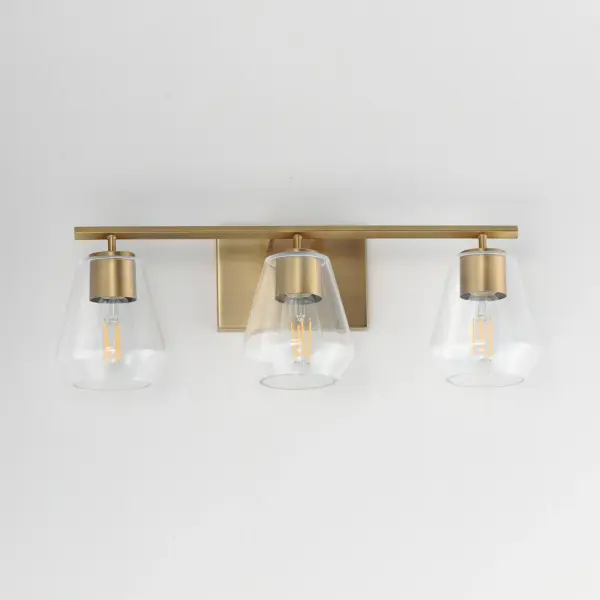 Crystalline clarity meets modern structure in the Geode collection. Inspired by the faceted symmetry of natural mineral formations, each clear glass shade is cut in an angular form that plays with light and shadow. The bold, geometric silhouette feels effortlessly architectural -- elevated further by subtle industrial notes like knurled screw collars and diamond shaped tubing on bath configurations. Offered in a range of sizes and finishes, Geode brings sculptural interest to kitchens, bathrooms, and dining rooms as well as statement-making entryways. Collection: Geode Finish: Natural Aged Brass Glass: Clear Width: 22.50" Height: 7.75" Weight: 4.40 lb Extension from Wall: 6.50" Wire: 8" Canopy: 4.75"x7" Number of Bulbs: 3 Maximum Wattage: 60.00 W Bulb Type: A19 Bulb Base: E26 Medium Light Source: Incandescent Voltage: 120.00 V Material: Steel, Glass Safety Listing: cULus Safety Rating: Damp Manufacturer Warranty: 3 Spec Sheet - alternate view