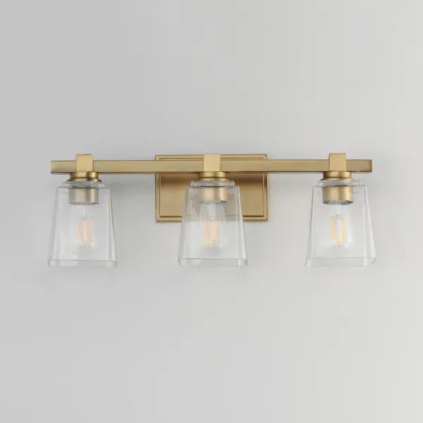 A composition of square forms that feature a Clear tapered square glass shade, these bath vanities provide a transitional design that suits both modern and traditional spaces. Available in Matte Black, Polished Chrome, Satin Nickel, and Natural Aged Brass. Collection: Cubos Finish: Natural Aged Brass Glass: Clear Width: 22.25" Height: 8.00" Weight: 6.30 lb Extension from Wall: 6.00" Wire: 8" Canopy: 4.75"x7.75" Number of Bulbs: 3 Maximum Wattage: 60.00 W Bulb Type: A19 Bulb Base: E26 Medium Light Source: Incandescent Dimmable Voltage: 120.00 V Material: Steel, Glass Safety Listing: cULus Safety Rating: Damp Manufacturer Warranty: 3 Spec Sheet Instructions - alternate view
