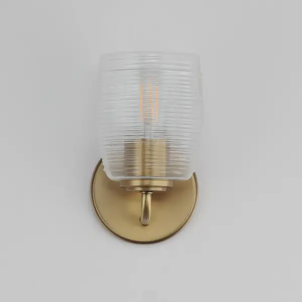 Warm and subtly nostalgic, the Honey collection draws inspiration from vintage honey jars and the familiar grooves of wooden dippers. Delicate ribbing on the clear glass shades plays with the light, creating gentle refractions that echo the soft sweetness of its namesake. Finished in either hand-brushed Kentucky Bronze or Natural Aged Brass, the frame brings an inviting glow that suits both traditional and contemporary settings. Honey lends an effortless charm to vanities, powder rooms, or anywhere you want a little golden-hour warmth--any time of day. Collection: Honey Finish: Natural Aged Brass Glass: Clear Ribbed Width: 5.00" Height: 8.50" Weight: 2.65 lb Extension from Wall: 6.00" Wire: 8" Canopy: 5"x5" Number of Bulbs: 1 Maximum Wattage: 60.00 W Bulb Type: A19 Bulb Base: E26 Medium Light Source: Incandescent Voltage: 120.00 V Material: Steel, Glass Safety Listing: cULus Safety Rating: Damp Manufacturer Warranty: 3 Spec Sheet - alternate view