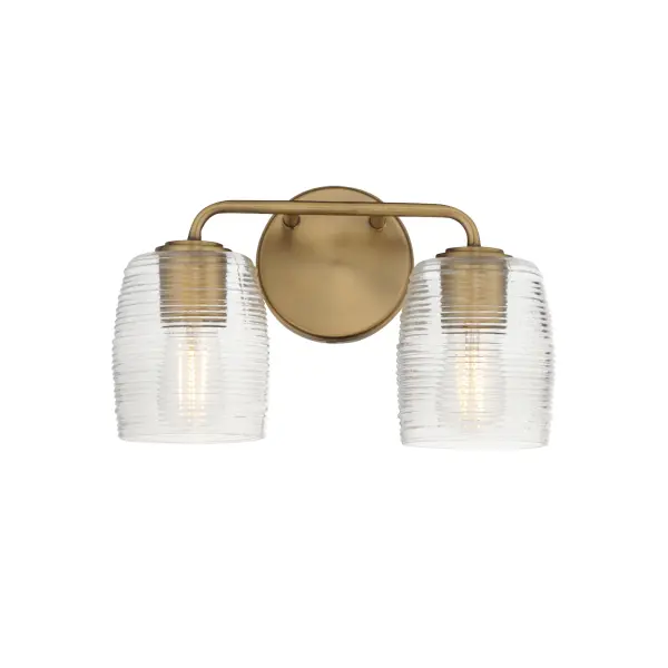 Warm and subtly nostalgic, the Honey collection draws inspiration from vintage honey jars and the familiar grooves of wooden dippers. Delicate ribbing on the clear glass shades plays with the light, creating gentle refractions that echo the soft sweetness of its namesake. Finished in either hand-brushed Kentucky Bronze or Natural Aged Brass, the frame brings an inviting glow that suits both traditional and contemporary settings. Honey lends an effortless charm to vanities, powder rooms, or anywhere you want a little golden-hour warmth--any time of day. Collection: Honey Finish: Natural Aged Brass Glass: Clear Ribbed Width: 14.00" Height: 8.25" Weight: 3.70 lb Extension from Wall: 6.00" Wire: 8" Canopy: 5"x5" Number of Bulbs: 2 Maximum Wattage: 60.00 W Bulb Type: A19 Bulb Base: E26 Medium Light Source: Incandescent Voltage: 120.00 V Material: Steel, Glass Safety Listing: cULus Safety Rating: Damp Manufacturer Warranty: 3 Spec Sheet
