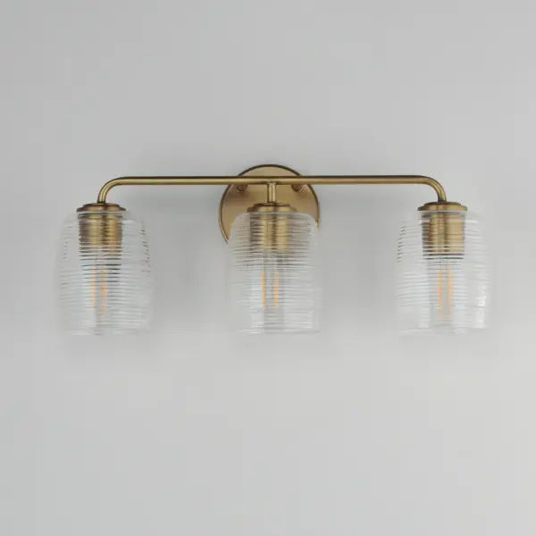 Warm and subtly nostalgic, the Honey collection draws inspiration from vintage honey jars and the familiar grooves of wooden dippers. Delicate ribbing on the clear glass shades plays with the light, creating gentle refractions that echo the soft sweetness of its namesake. Finished in either hand-brushed Kentucky Bronze or Natural Aged Brass, the frame brings an inviting glow that suits both traditional and contemporary settings. Honey lends an effortless charm to vanities, powder rooms, or anywhere you want a little golden-hour warmth--any time of day. Collection: Honey Finish: Natural Aged Brass Glass: Clear Ribbed Width: 22.00" Height: 8.50" Weight: 5.50 lb Extension from Wall: 6.00" Wire: 8" Canopy: 5"x5" Number of Bulbs: 3 Maximum Wattage: 60.00 W Bulb Type: A19 Bulb Base: E26 Medium Light Source: Incandescent Voltage: 120.00 V Material: Steel, Glass Safety Listing: cULus Safety Rating: Damp Manufacturer Warranty: 3 Spec Sheet - alternate view