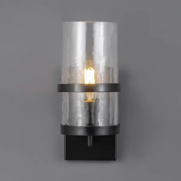Rugged yet refined, Chamberlain pairs clean lines with a handcrafted feel. A thick glass cylinder, beautiful in its subtle imperfection, diffuses light with soft ripples and warmth. Dark Bronze strapping adds architectural structure, grounding the design while gently shielding glare. Finished in a weather-resistant powder coat, Chamberlain is made to elevate exteriors with understated elegance. - alternate view