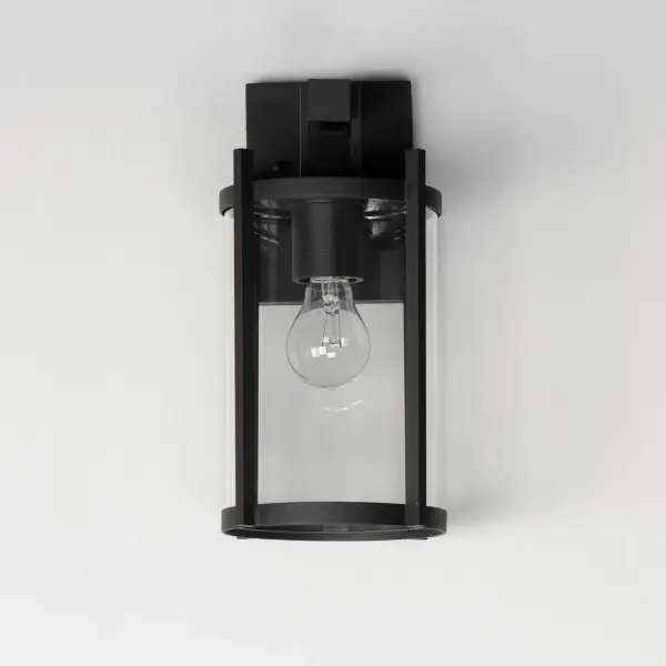 Squared columns in Matte Black finish tower above the cylindrical glass shade rated for outdoor applications. Available in a more modern clear glass option or hammered glass. A rectangular hook detail carries the square form through to the backplate. A modern interpretation of a bell tower, these outdoor pendants and sconces are a cleaned up, transitional look for exteriors. - alternate view