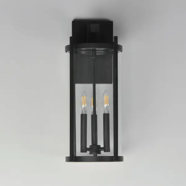 Squared columns in Matte Black finish tower above the cylindrical glass shade rated for outdoor applications. Available in a more modern clear glass option or hammered glass. A rectangular hook detail carries the square form through to the backplate. A modern interpretation of a bell tower, these outdoor pendants and sconces are a cleaned up, transitional look for exteriors. - alternate view