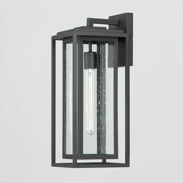 A dual framed structure creates dimension on these outdoor lighting fixtures that is both contemporary and transitional. The construction consists of two frames of square tubing and squared components. The inner frame's Clear Seedy glass reduces glare from the light and appears dirt-free for longer periods. This is a comprehensive collection to brighten all areas of your outdoor space, available in various sized sconces as well as hanging and post configurations. - alternate view