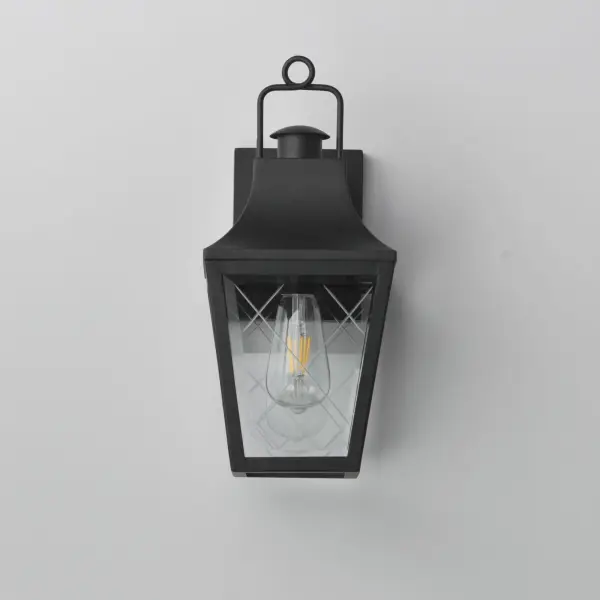 These charming cottage style lanterns feature unique cross-etched glass panels that are Clear and beveled along their edges. Additional design details such as whimsical loops above a chimney element add to the product's delightful appearance. Finished in a Matte Black outdoor rated powder coat, this collection recaptures the appeal of storybook lanterns. - alternate view