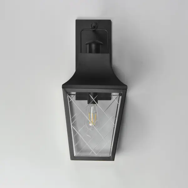 These charming cottage style lanterns feature unique cross-etched glass panels that are Clear and beveled along their edges. Additional design details such as whimsical loops above a chimney element add to the product's delightful appearance. Finished in a Matte Black outdoor rated powder coat, this collection recaptures the appeal of storybook lanterns. - alternate view