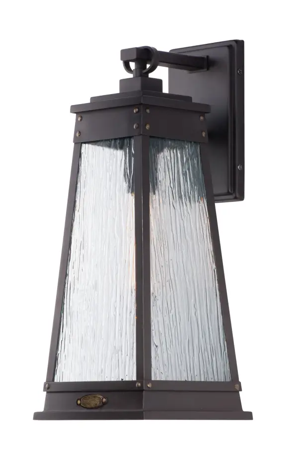 A tapered square shade finished in Olde Brass suspends from a bracket to replicate a nautical lantern. Panels of clear Ripple glass allow for the lamp to shine through while still diffusing the light. The medallion at the base of the shade and rivets along the frame are finished in an antique brass to add authenticity to the design.