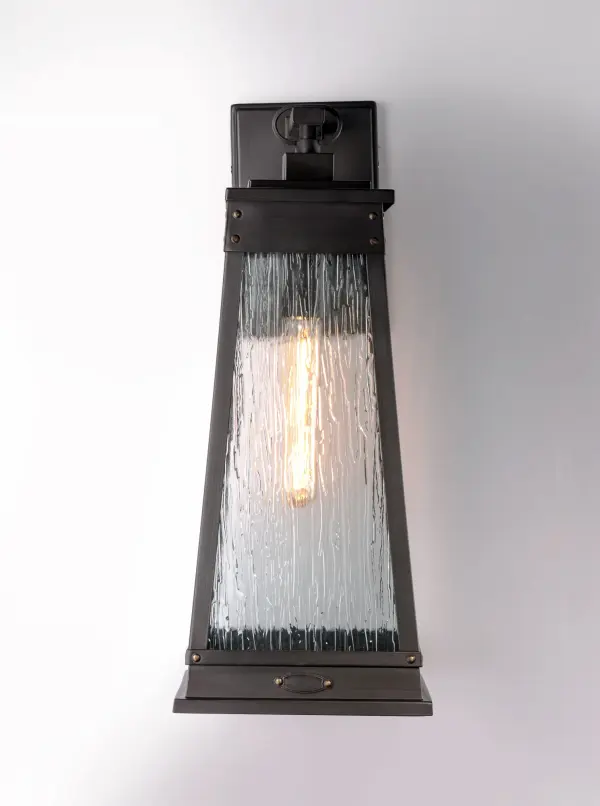 A tapered square shade finished in Olde Brass suspends from a bracket to replicate a nautical lantern. Panels of clear Ripple glass allow for the lamp to shine through while still diffusing the light. The medallion at the base of the shade and rivets along the frame are finished in an antique brass to add authenticity to the design. - alternate view