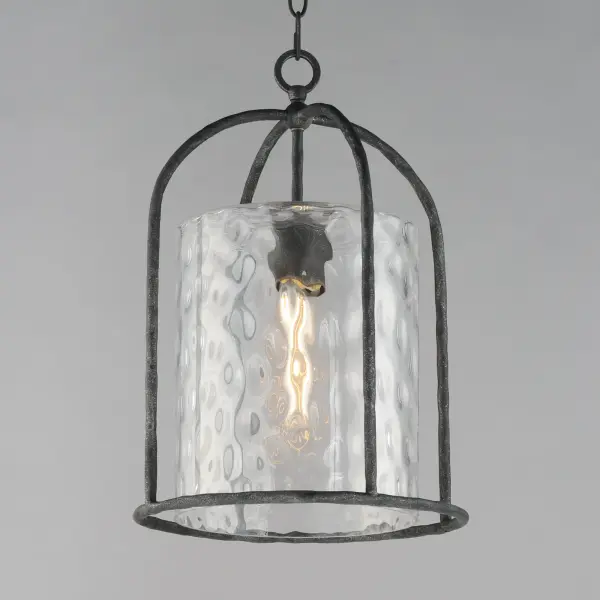 Inspired by classic European lanterns and handcrafted ironwork, the Del Mar collection brings timeless sophistication to exterior spaces. Its airy open-frame silhouette is crafted of hammered iron, elegantly arched with a graceful hook detail that nods to historic gas lamps. Inside the frame, a delicate Water glass cylinder shimmers with texture, diffusing light in a soft, atmospheric glow. Designed for lasting beauty in the elements, each piece is finished in a richly layered Blacksmith finish--a deep near-black tone highlighted by silvery brushstrokes, adding artisanal character to the silhouette. Whether flanking a grand entry or lining a garden path, Del Mar offers a refined approach to outdoor lighting with enduring presence. - alternate view