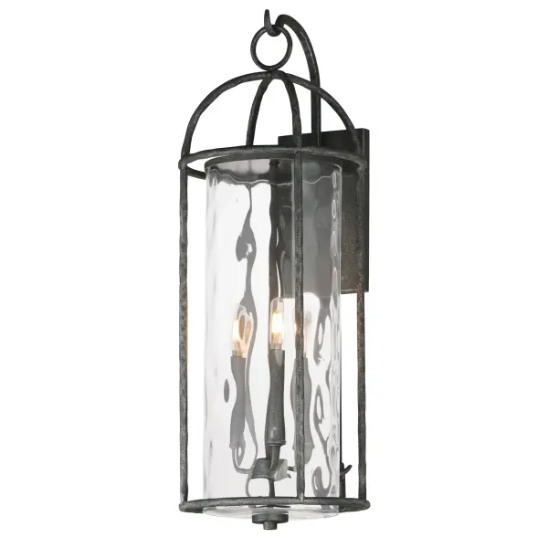 Inspired by classic European lanterns and handcrafted ironwork, the Del Mar collection brings timeless sophistication to exterior spaces. Its airy open-frame silhouette is crafted of hammered iron, elegantly arched with a graceful hook detail that nods to historic gas lamps. Inside the frame, a delicate Water glass cylinder shimmers with texture, diffusing light in a soft, atmospheric glow. Designed for lasting beauty in the elements, each piece is finished in a richly layered Blacksmith finish--a deep near-black tone highlighted by silvery brushstrokes, adding artisanal character to the silhouette. Whether flanking a grand entry or lining a garden path, Del Mar offers a refined approach to outdoor lighting with enduring presence.