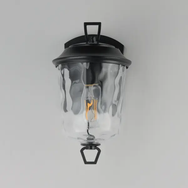 The Prescott collection of outdoor lanterns reimagines a classic design with timeless elegance. Crafted with a durable die-cast aluminum frame and finished in a sleek Matte Black, these lanterns exude a refined, understated charm. The water glass shade creates a beautiful lighting effect as it casts dazzling patterns on its surrounding surfaces. Thoughtfully updated with simple stirrup hook details, the collection effortlessly blends tradition with modern sophistication. - alternate view