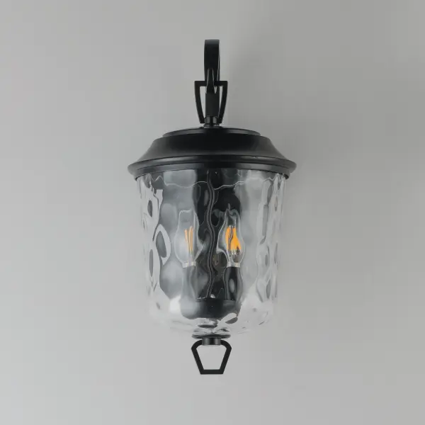 The Prescott collection of outdoor lanterns reimagines a classic design with timeless elegance. Crafted with a durable die-cast aluminum frame and finished in a sleek Matte Black, these lanterns exude a refined, understated charm. The water glass shade creates a beautiful lighting effect as it casts dazzling patterns on its surrounding surfaces. Thoughtfully updated with simple stirrup hook details, the collection effortlessly blends tradition with modern sophistication. - alternate view