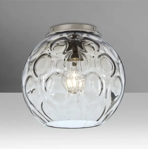 The Bombay semi-flush mount features a clear glass globe with circular optical patterns that create dramatic light play across surfaces. The visible filament adds warmth while the textured glass provides visual interest.