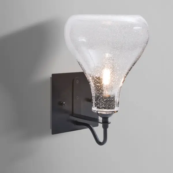 The Melo Clear Bubble Sconce combines timeless design with artisanal glass craftsmanship. Its transparent bubble-patterned shade and classic gooseneck arm create striking light play while showcasing decorative filament bulbs.