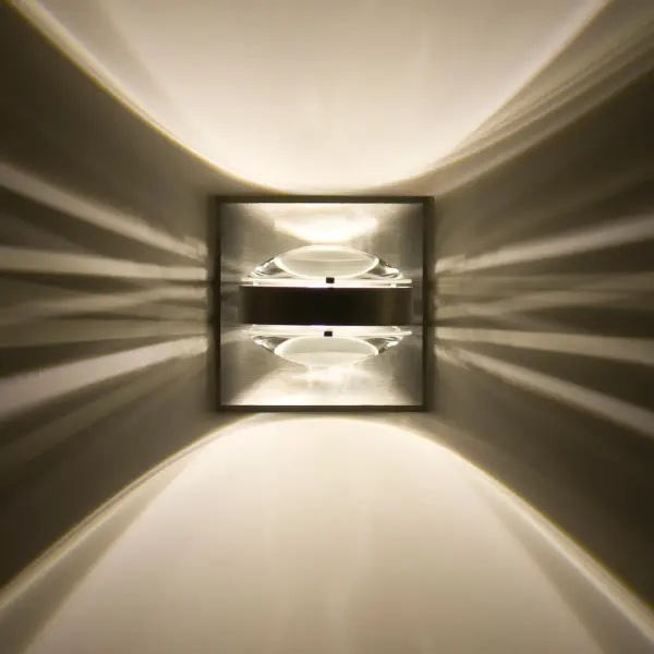 The Optos wall sconce features dual optical-effect lenses that create striking up/down light patterns. With 359-degree rotation capability and handcrafted borosilicate glass lenses, it delivers functional illumination with contemporary flair.