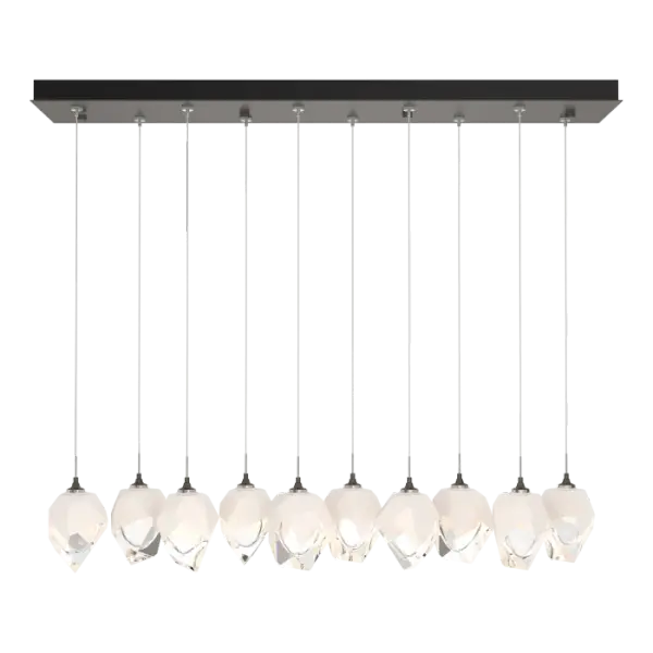 The Chrysalis 10-Light Small Crystal Pendant is a multi-port fixture that features ten small, handcrafted faceted glass crystals suspended from a rectangular canopy. A thick, clear layer of glass is encased in an outer cocoon of hand-blown, colored glass (matte black or white; all 10 are same color). Hand-polished like a gemstone, the lower portion of the outer layer of glass is removed to reveal the inner crystal clear layer below. Each crystal is lit from within.