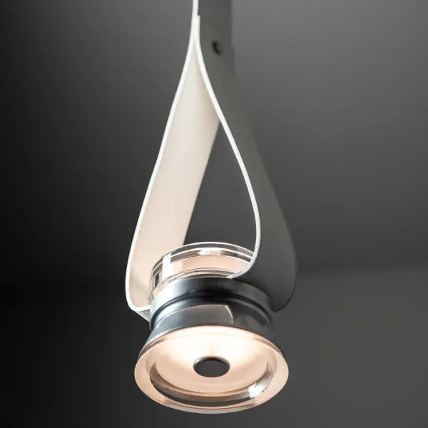 This original design features a simple 1-light, downward-facing glass partially encased in a metal cone-shaped housing that leaves exposed the top and bottom portions of this thick, clear, shaped glass. The leather strap is elegantly looped above it, creating a vision of void with the elements. The LED components are diffused by an inner "puck" and with frosted glass at the center of the downlight. The fine grain leather strap is offered in a choice of 3 standard colors. Custom color options are available. - alternate view