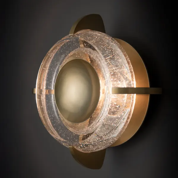 The depth of the gently curved, heavy handmade bubble glass gives a glimpse of the richness of this elegant wall sconce. The Lustra's central metal disc gives a concave "saucer" effect, drawing the eye to the unique and stunning glass surround. Can also be mounted to the ceiling as a small flush mount.