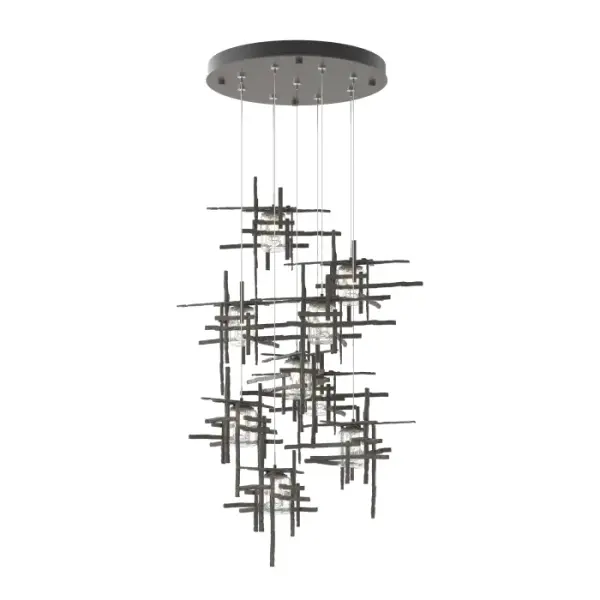 A show-stopping design, the Tura's perpendicular, intersecting metal pieces are crafted from annealed aluminum that are hand textured using a trip hammer and custom dies by Vermont artisans. Nine pendants are each customizable in length on a round canopy to create the ideal staggered effect to suit its space. Shades are made of double layers of thick, clear, seeded glass. The Tura 9-Light multi-port chandelier is a stunning focal point, and available in all standard finishes.