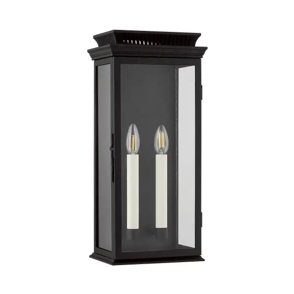 The Louie wall sconce brings vintage lantern charm to outdoor spaces with its box-shaped frame, clear glass panels, and decorative chimney detail. The forged iron finish and candlestick-style lighting create warm ambiance.