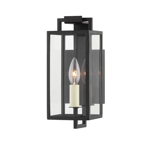 The Beckham sconce combines traditional lantern styling with an elongated modern silhouette. Its forged iron finish and clear glass panels create ambient lighting ideal for grand exterior spaces.