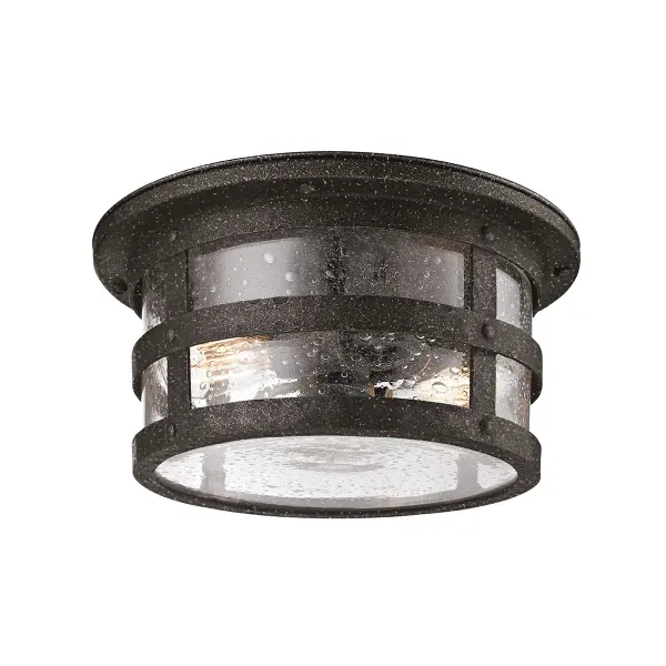 The Barbosa flush mount combines hand-forged iron construction with clear seeded glass for authentic industrial character. Its low-profile design and damp rating make it ideal for covered outdoor spaces and transitional areas.